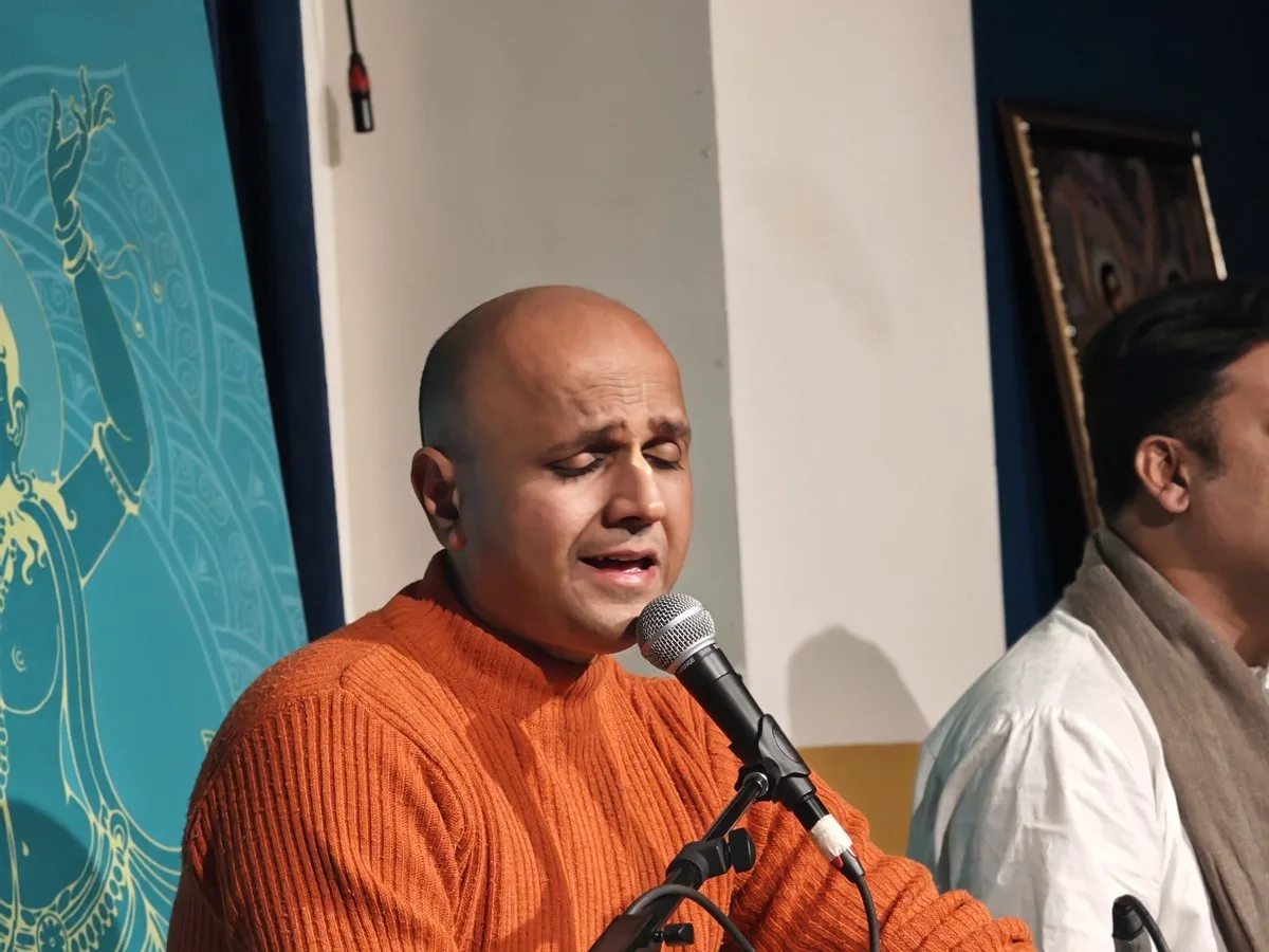 A kirtan singer at the microphone beside teal Krishna artwork