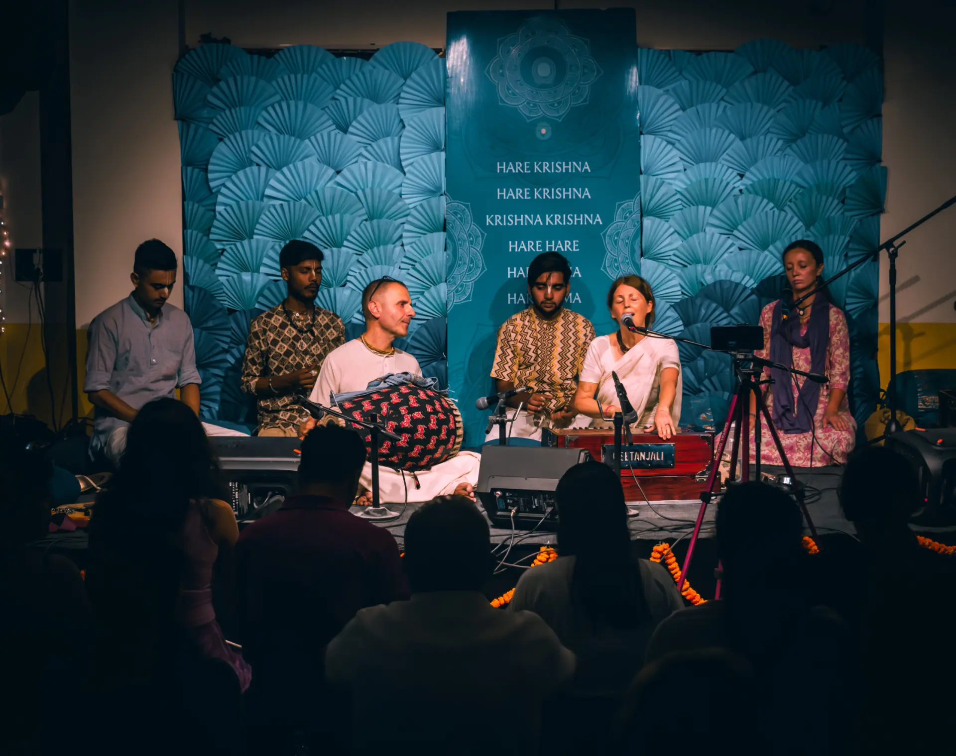 The kirtan ensemble on stage beneath the Hare Krishna mantra at Kirtan Mela