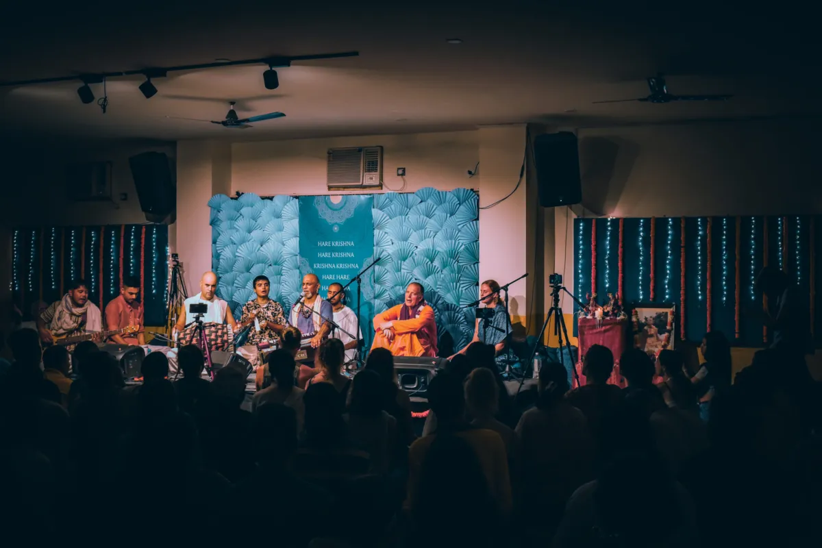 Kirtan singers on stage before the teal Hare Krishna backdrop at Kirtan Mela
